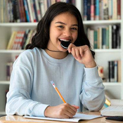 Teenager girl chewing oreo anxiety necklace in black. Holding chewable pencil topper.