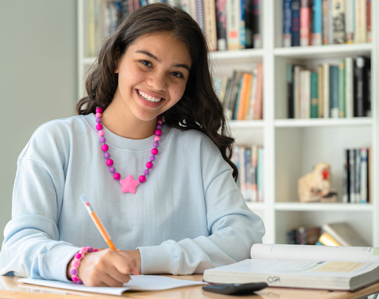 Teenager girl uses pencil with discreet clear chewy tube pencil topper. Also wears Starlight Chewelry and a chewable bracelet