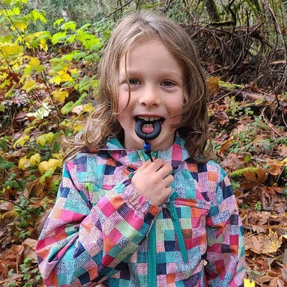 Girl chewing on Munchables Black Donut Chewable Zipper Pull.