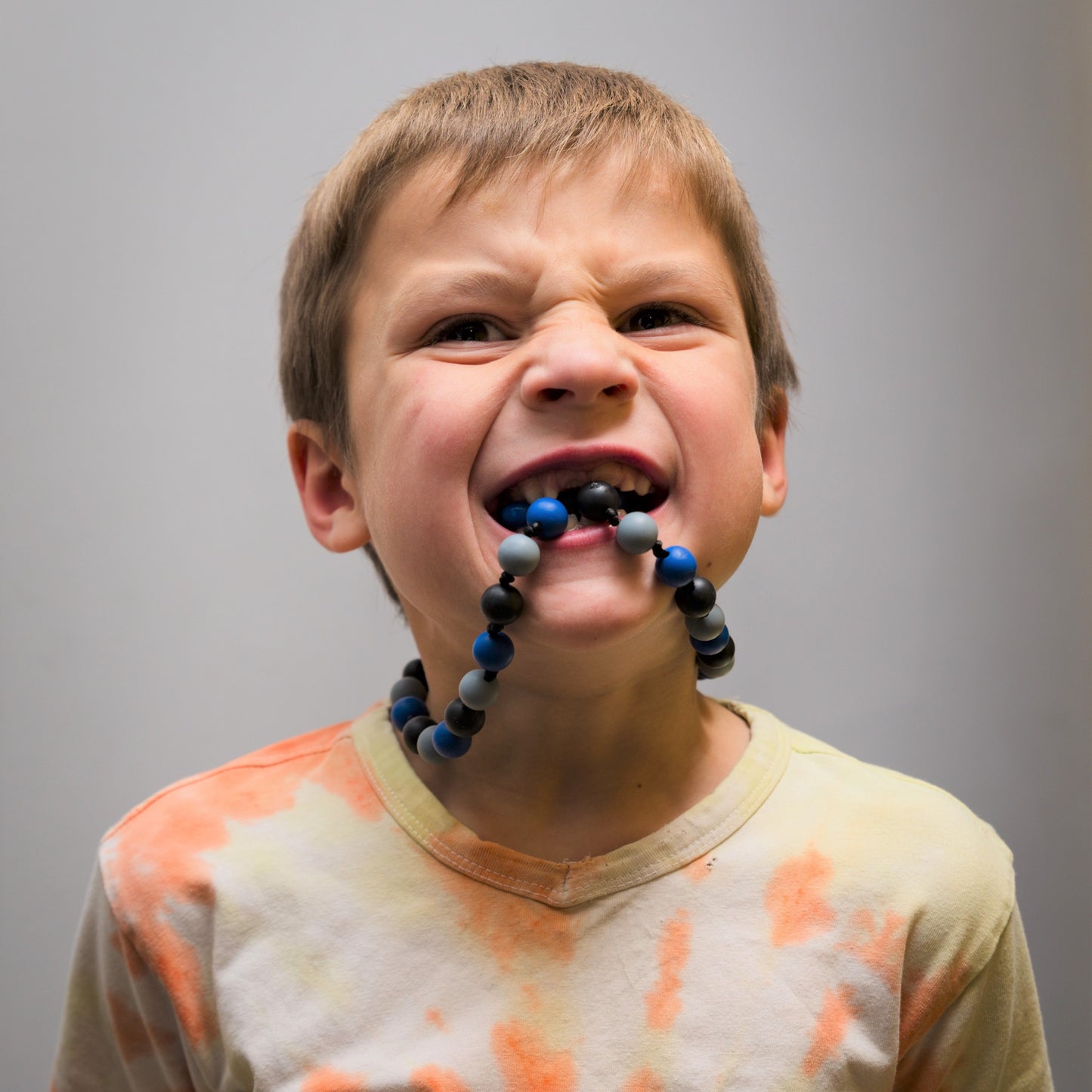 Boy gnawing on anxiety necklace. In mouth.